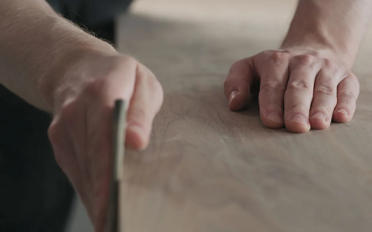 ZNahaufnahme einer Hand, die eine Holzoberfläche bearbeitet. Symbol für handwerkliche Qualität, Präzision und Liebe zum Detail im modernen Küchenbau.